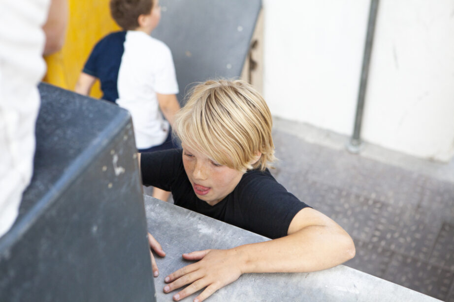 Kind übt im Stuntwerk Essen eine Parkour-Hindernisüberwindung und zieht sich an einer Kante hoch. Spielerisches Training von Kraft, Koordination und Beweglichkeit im Kinderbereich.