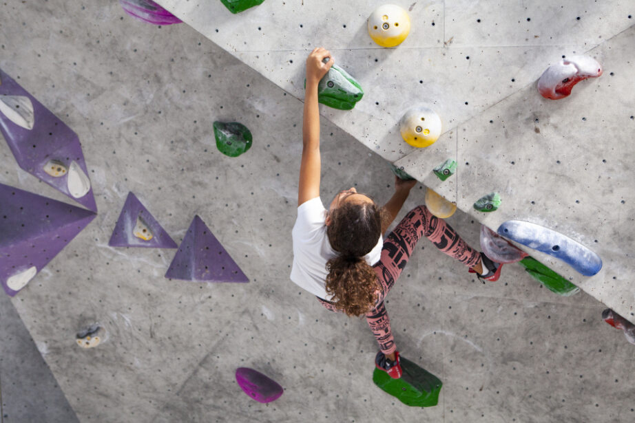 Kind bouldert im Stuntwerk Essen an einer farbigen Kletterwand. Sichere Bewegungen an kindgerechten Griffen, Förderung von Koordination und Kraft.